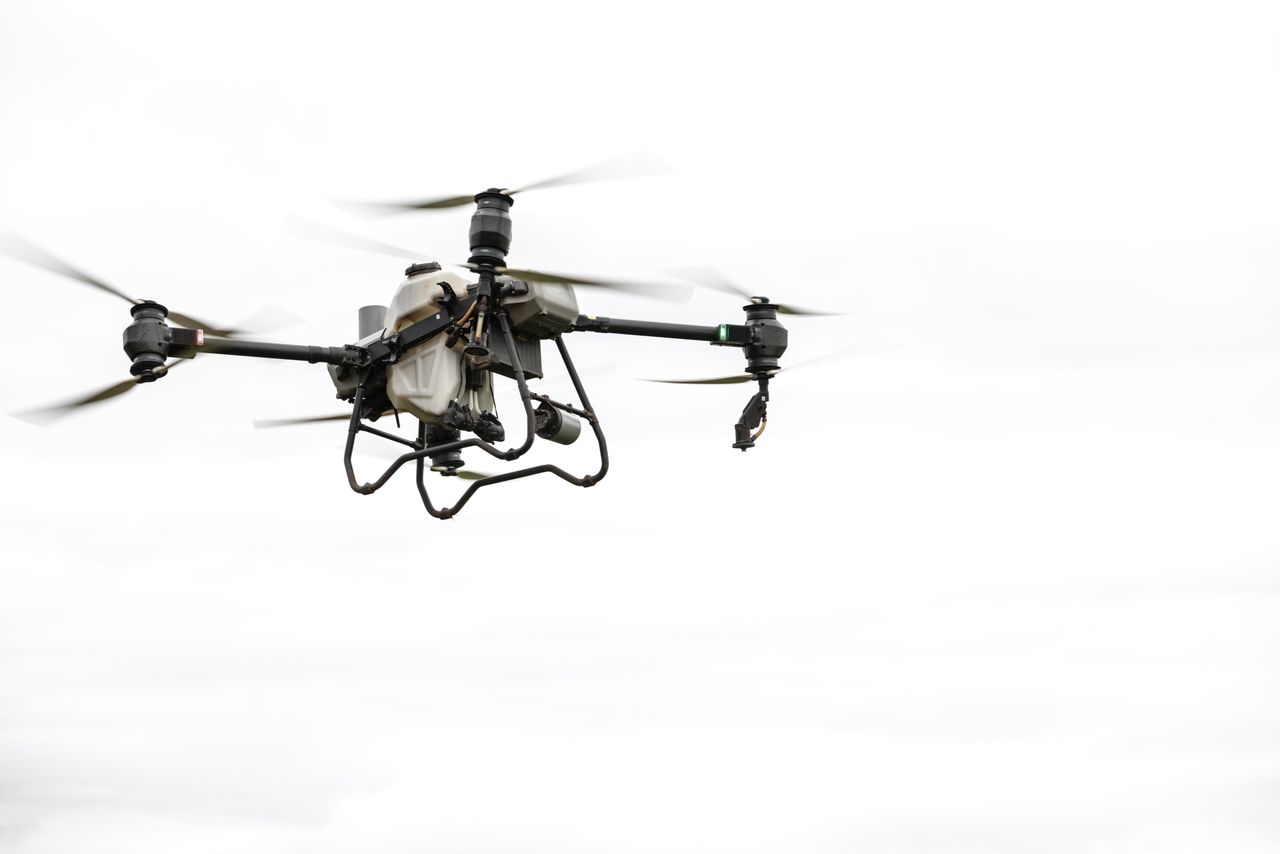 High-tech agricultural drone in flight against a cloudy sky, showcasing modern farming technology.