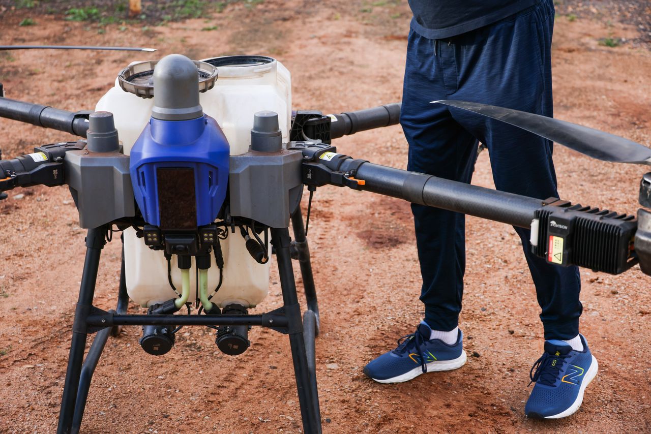 Close-up of an agricultural drone in use on a dirt field, piloted by a person.